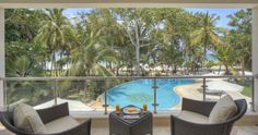 two wicker chairs sitting on top of a balcony next to a pool and palm trees