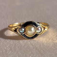 Antique 18k yellow gold ring from the United Kingdom c 1864. This Victorian piece is part of the mourning jewelry movement of the time. The heirloom features three pearls and enamel surrounding the face of the ring. Within the ring, the words "Mary-Ann Buckle died Oct 7, 1864". Great antique condition Size: 5.25 - 5 Weight: 2.0 grams Band: 7.2 mm (front), 1.3 mm (back) Pearls: 3.5 mm x pearl, 2.0 mm x 2 pearls Antique Gold Enamel Ring With Rose Cut Diamonds, Victorian Enamel Ring For Anniversary, Vintage Black Enamel Ring For Anniversary, Victorian Yellow Gold Enamel Ring For Anniversary, Vintage Gold Enamel Ring With Rose Cut Diamonds, Vintage Yellow Gold Enamel Ring With Rose Cut Diamonds, Yellow Gold Black Enamel Wedding Ring, Wedding Yellow Gold Enamel Ring With Black Detail, Wedding Yellow Gold Ring With Black Enamel