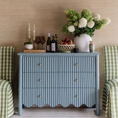 a blue dresser sitting next to two green checkered chairs and a white vase with flowers