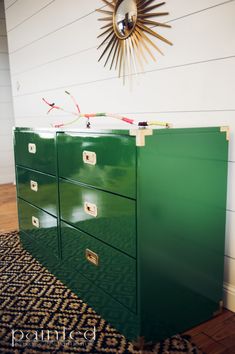 a green dresser sitting on top of a wooden floor next to a sunburst