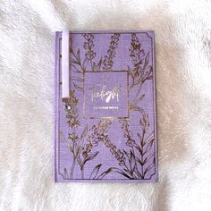 a purple notebook sitting on top of a white furnishce covered floor next to a pen