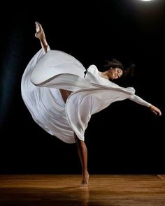 a woman in white is dancing on a wooden floor with her arms spread out and legs extended