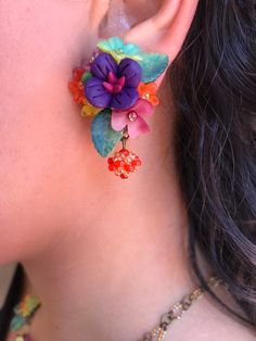 Gorgeous little petunia earring with a central purple polymer clay flower mixed with a striking color combo of red, orange, green and yellow. These earrings are hand sewn together with glass beads and hand painted resin flowers, finished off with a pretty handbeaded bauble. This is a quality piece of jewelry that will last a life time. Created by designer Colleen Toland who has been creating her unique style of vintage jewelry for more than 30 years. All of our pieces come with an engraved tag w Multicolor Flower-shaped Earrings With Colorful Beads, Whimsical Multicolor Flower Charm Earrings, Handmade Colorful Flower Earrings, Handmade Multicolor Flower Earrings, Multicolor Handmade Flower Earrings, Multicolor 3d Flower Earrings, Unique Multicolor Flower-shaped Beaded Earrings, Bohemian Multicolor Hand Painted Flower Earrings, Whimsical Handmade Multicolor Beaded Earrings