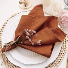 napkins with dried flowers on them sit on a plate next to other place settings