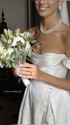 a woman in a white dress holding a bouquet of flowers and pearls on her wedding day