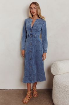 a woman standing in front of a wall wearing a denim dress