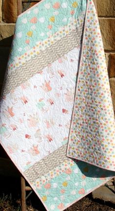 two baby quilts sitting next to each other on top of a wooden chair in front of a brick wall