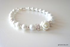 a bracelet with white pearls and crystal flowers on it's end, sitting on a table