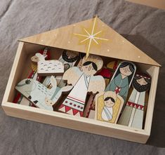 a wooden nativity set in a box on a bed with grey sheets and a star above it