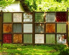 a fence made out of old windows in the grass with trees and bushes behind it