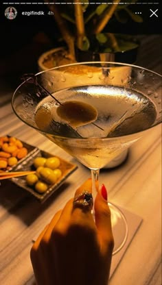 a woman is holding a martini glass with olives in it