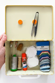 someone is holding an open sewing box with scissors and other crafting supplies in it