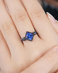 a woman's hand with a blue ring on top of her finger and an engagement ring in the middle