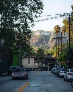 cars are parked on the street in front of houses and trees with hollywood sign above them