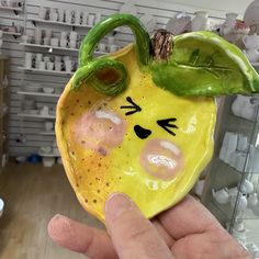 a hand holding a yellow ceramic fruit with eyes and nose painted on it's face