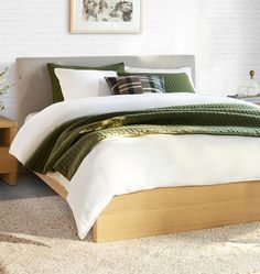 a bed with green and white pillows in a room next to a wall mounted painting