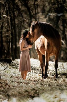 a woman standing next to a brown horse in the woods with snow on the ground