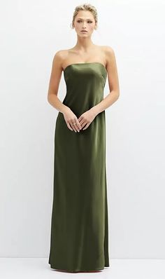 a woman in a green strapless dress standing against a white wall with her hands on her hips