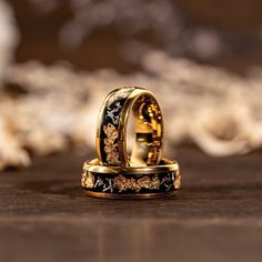 two gold wedding rings sitting on top of each other with black and white flowers in the middle