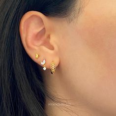 a close up of a person's ear wearing gold and silver earrings with leaves on them