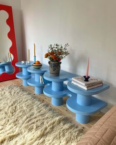 a room with a bed, mirror and blue tables in front of a white wall