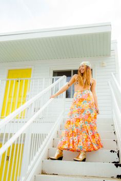 Model poses in a 70s retro floral print maxi skirt. The neon colors stand out against the white reto motel stairs. Retro Floral Print Bottoms For Vacation, Vintage Summer Vacation Skirt, Vintage Tiered Skirt For Summer, Multicolor Retro Skirt For Vacation, Vintage Floral Print Bottoms For Vacation, Retro Multicolor Skirt For Vacation, Vintage Tiered Skirt For The Beach, Vintage Floral Print Tiered Skirt, Vintage Tiered Skirt Bottoms For Festival