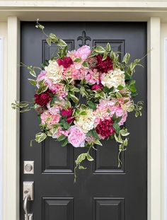 a black front door with pink and white flowers hanging from it's side frame