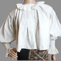 This is an antique Romanian blouse, originating from Transylvania, Bihor and crafted by hand, most likely between the 1930s and 1960s. The blouse is constructed from a thick, hand-woven fabric, resembling denim, and is adorned with stunning white cotton hand embroidery on the shoulders, cuffs, chest and ruffles . This particular blouse is versatile and can fit sizes XXS-XS, as well as German sizes 34-36.  The neck measures 33 cm (13 inches), while the distance from neck to shoulder seam is 14 cm (5.5 inches), and the circumference around the shoulder seam is 36 cm (14.17 inches). Additionally, the sleeve length from the neck measures 58 cm (22.8 inches), complete with a frill of 7 cm (2.75 inches). From armpit to armpit, the blouse measures 62 cm (24.4 inches), and has a length of 49 cm (1 Cotton Long Sleeve Costume Top, Peasant Style Cotton Blouse With Yoke, Peasant Style Cotton Blouse With Yoke Detail, Peasant Cotton Blouse With Ruffles, Cottagecore Style Cotton Blouse With Ruffled Collar, White Boho Collar Peasant Top, Cottagecore Cotton Blouse With Ruffled Collar, White Peasant Top With Boho Collar, Vintage Long Sleeve Costume Top