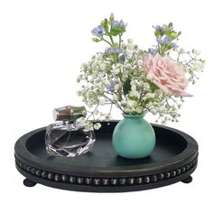 a blue vase with flowers and a perfume bottle sitting on a black tray that is holding it