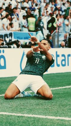 a soccer player sitting on the ground in front of a crowd with his hand up