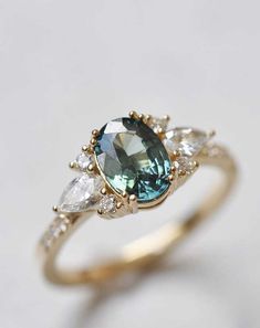 a blue and white diamond ring with three pear shaped diamonds on the side, set in yellow gold