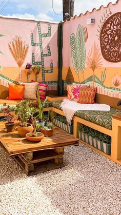 an outdoor seating area with potted plants and pillows on the bench, in front of a painted wall