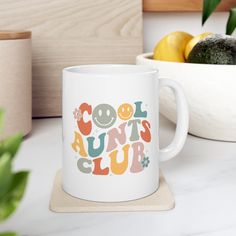 a white coffee mug sitting on top of a counter next to some fruit and vegetables