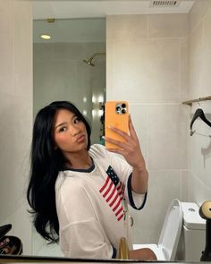 a woman taking a selfie in front of a bathroom mirror with an american flag t - shirt on