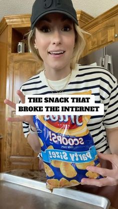 a woman in a black and white striped shirt is holding up a bag of chips