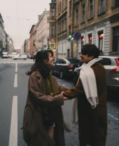 two people standing on the side of a road holding hands with each other in front of some parked cars