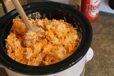 a crock pot filled with shredded cheese and a wooden spoon