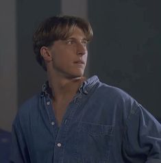 the young man is wearing a denim shirt and looking off into the distance with his hands in his pockets