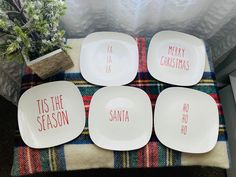 four white plates sitting on top of a plaid table cloth with merry christmas written on them