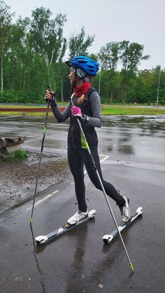 a woman riding skis across a wet parking lot holding poles and wearing a helmet