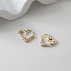 two gold heart shaped earrings sitting on top of a white table next to each other