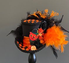 a black hat with orange feathers and a cat on it's side, sitting on top of a stand