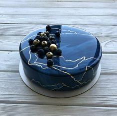 a blue cake with white and gold decorations sitting on top of a wooden table covered in frosting