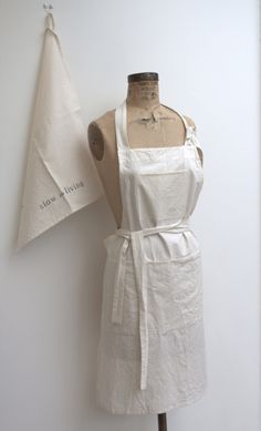 a white apron on a mannequin next to a piece of cloth that is hanging on a wall