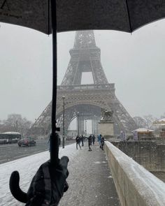 the eiffel tower is covered in snow as people walk under an open umbrella