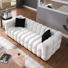 a large white couch sitting on top of a wooden floor next to a table with two black pillows