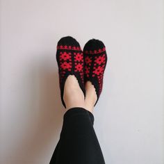 a person wearing slippers with red and black designs on them, standing next to a white wall