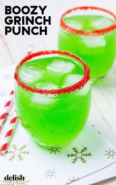 two glasses filled with boozy grin punch sitting on top of a table next to candy canes