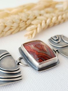 three pieces of silver and red glass on a white surface with some wheat in the background