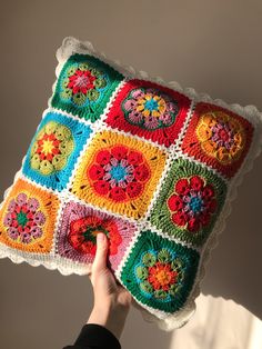 a person holding up a colorful crocheted pillow